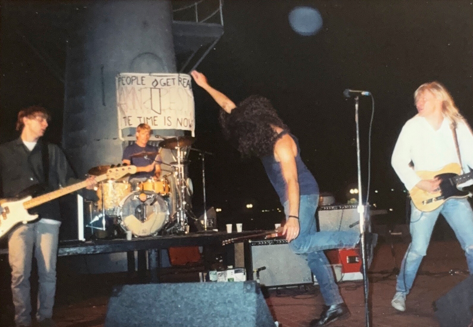 A bass player, drummer, singer (who is dancing here), and guitar player are performing a song.