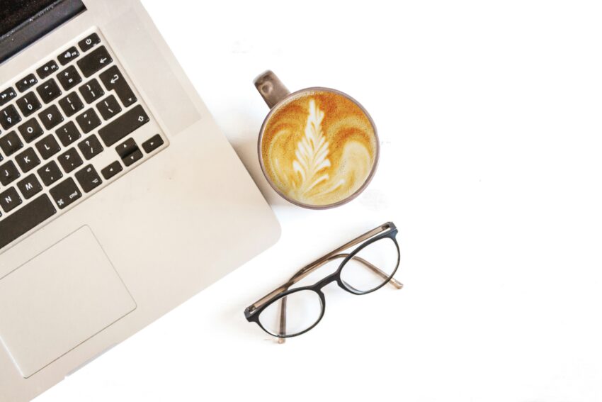 a silver laptop computer on a desk with a cup of coffee and a pair of glasses