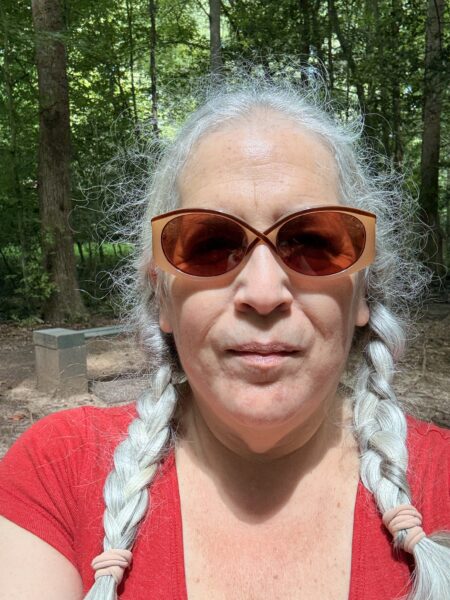 a woman with white hair in braids wearing sunglasses and a red shirt