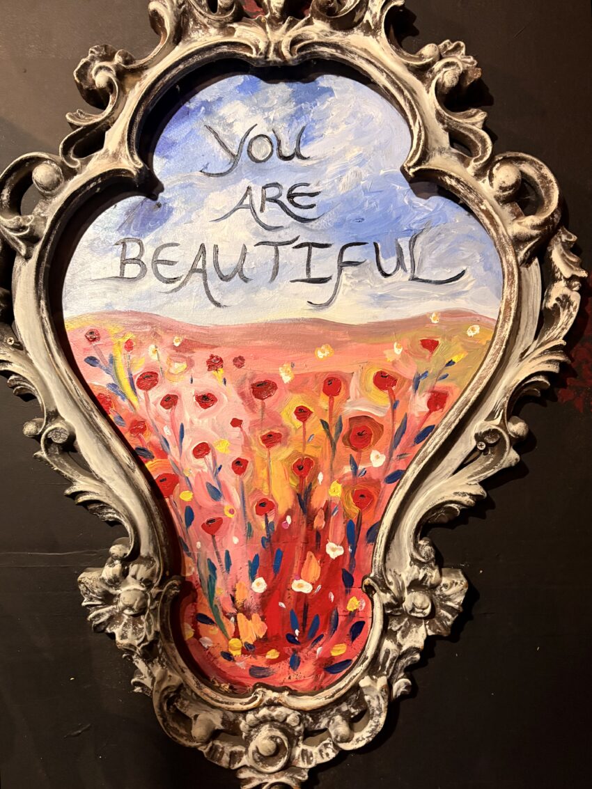 Artwork in the women's restroom at Cat's Cradle in Carrboro, NC, showing a field of red, pink, and yellow flowers with You Are Beautiful written in the sky