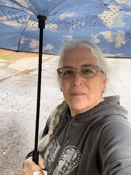 a woman wearing a grey hoodie and glasses holding an umbrella
