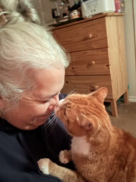 a woman with white hair getting kissed on her nose by her orange tabby