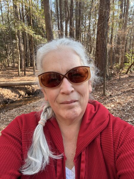 a woman with white hair in a single braid wearing a red hoodie and sunglasses on her first walk of 2026