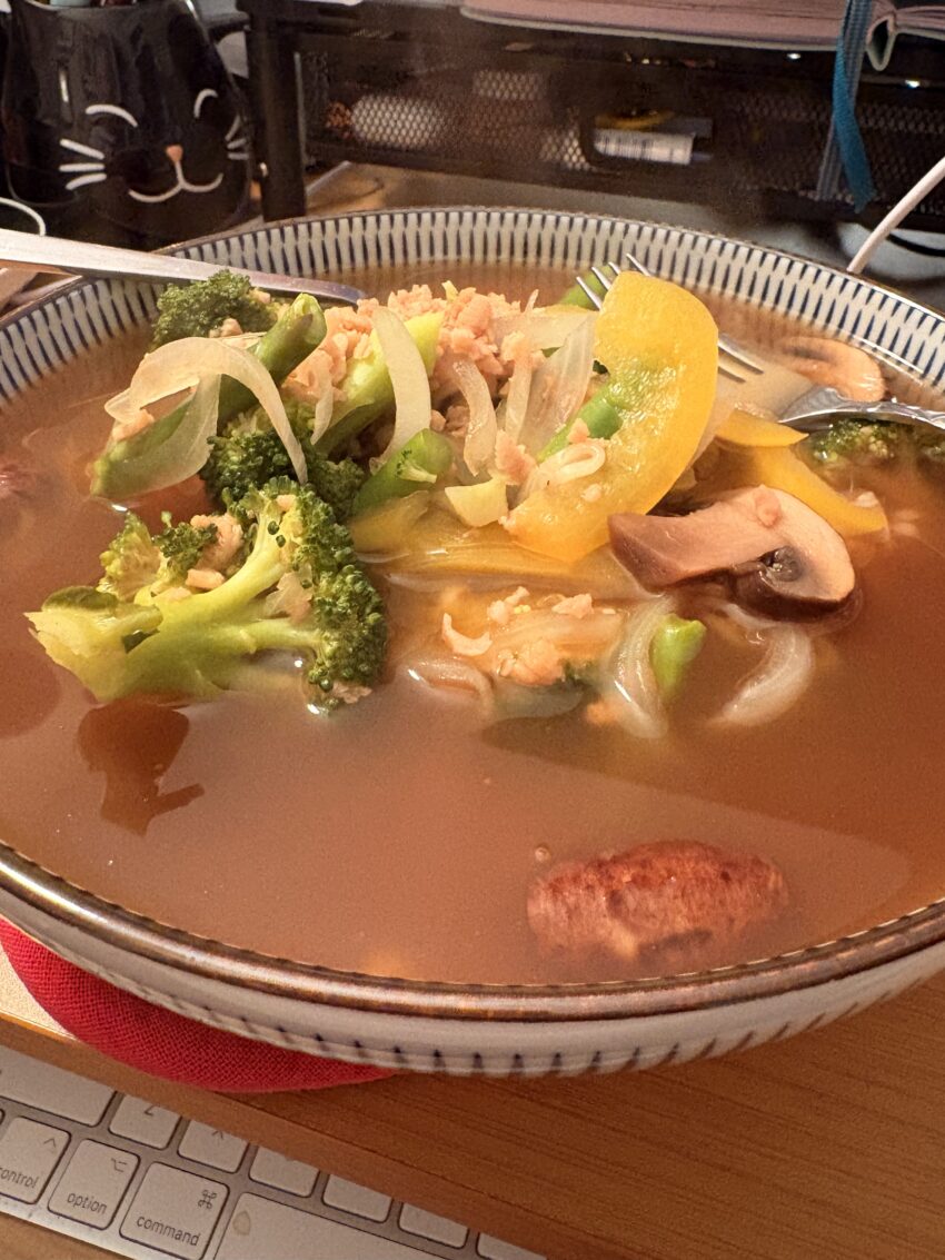 a bowl of ramen soup with broccoli, mushrooms, onion, yellow bell pepper, asparagus, textured vegan protein, and some actual ramen noodles